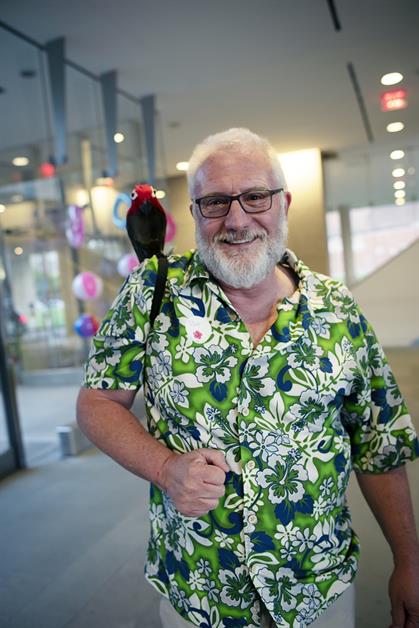 A man in a green, floral shirt smiles with a fake parrot on his shoulder