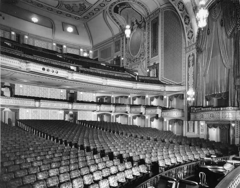 A black and white photo of the Orpheum Theater from 1928. Ornate seats and curtains adorn the concert hall