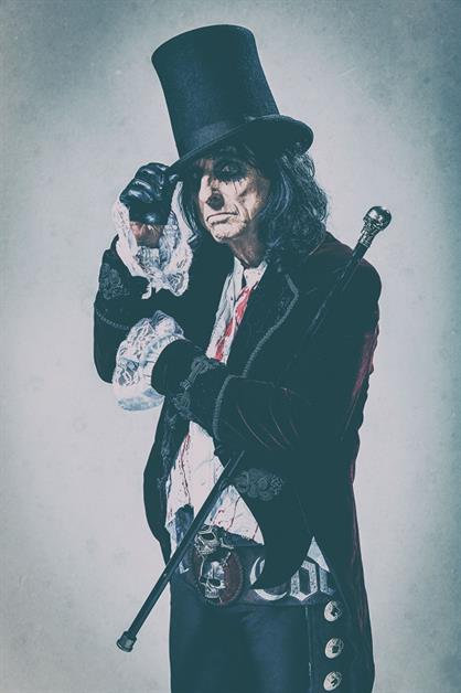 A man wears a top hat, velvet coat, lace shirt and carries a cane with a skull on top