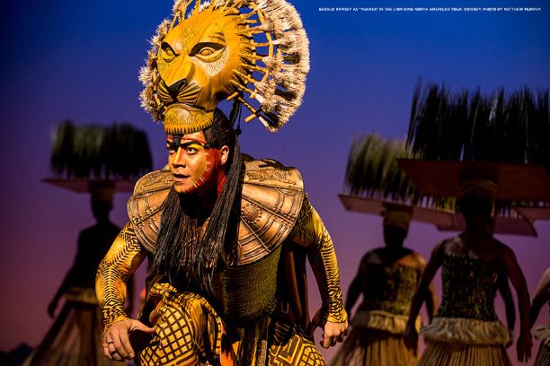 An actor with a lion headdress plays Mufasa on stage