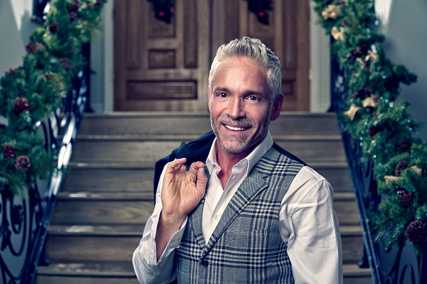 A well-dressed Dave Koz throws his suit jacket behind hist back whiles standing in front of a house stoop decorated for the holidays