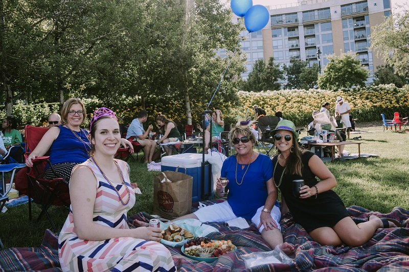 Four women sit on a picnic blanket with balloons in the background