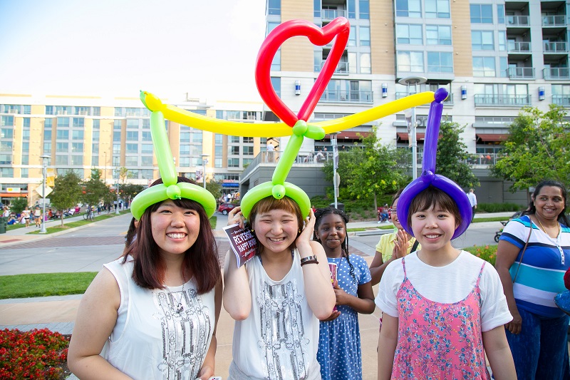 Three girls share a balloon hat, smiling and laughing
