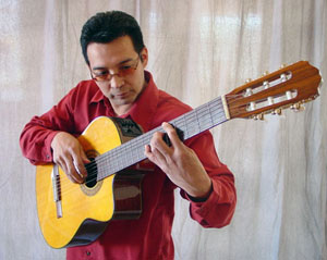 Marcos Mora, dressed in a red shirt and sunglasses, plays the guitar.