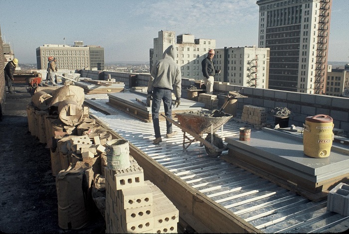 Men work on the roof of the theater. In the distance you can see the smaller Omaha skyline of the 1970s.